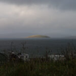 Small island under the sun with surrounding dark clouds