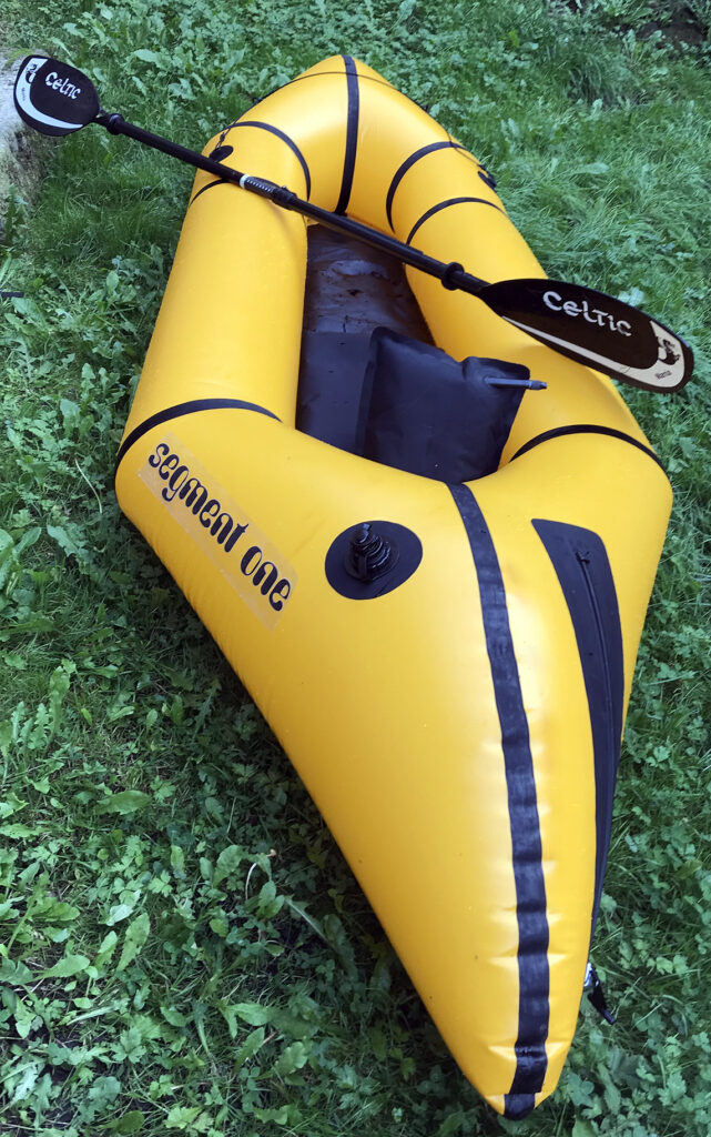 Inflated packraft and paddle on grass bank.