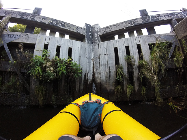 Front of packraft on canal in front of a lock gate.