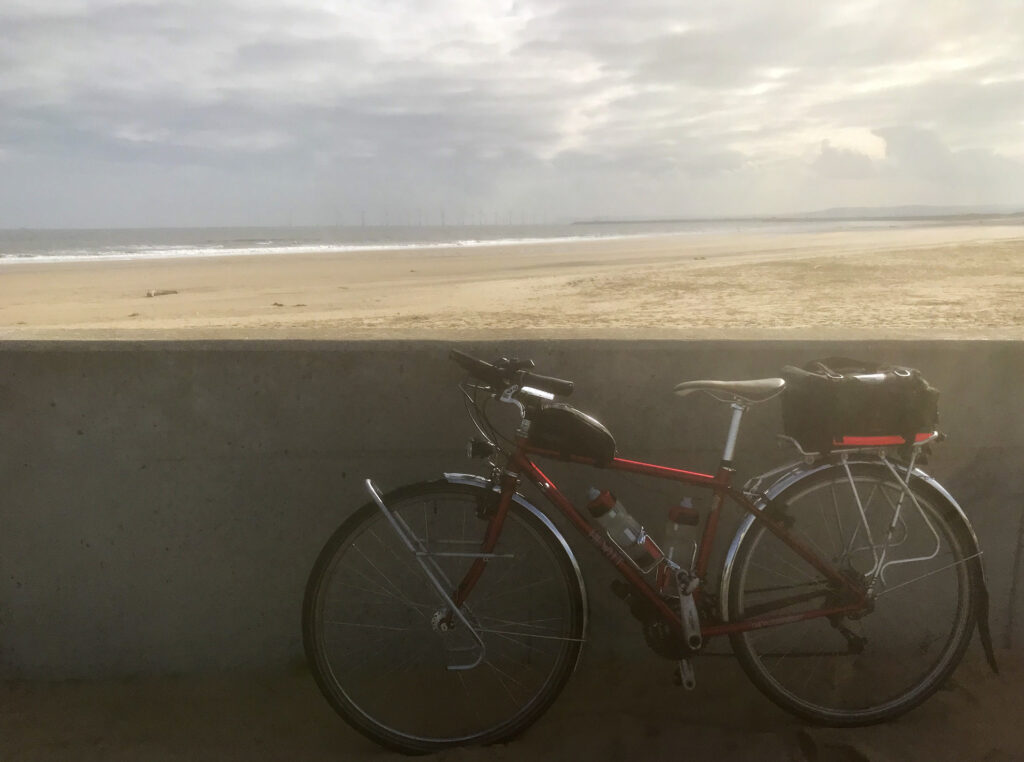 A bike resting on a seawall with a beach and sea in the distance
